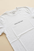 Light unisex T-shirt with 'merci, but non' quote, centered on a natural drape in a soft white studio setting.