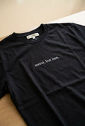 Unisex 'merci, but non' dark T-shirt with centered print on a neutral indoor surface.