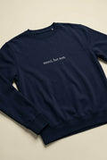 Photorealistic lifestyle shot of unisex organic sweatshirt with 'merci, but non.' slogan, front view, soft natural light, neutral indoor background.